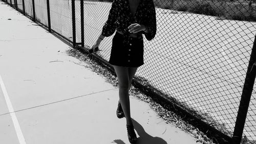 Low section of woman walking on street by chainlink fence