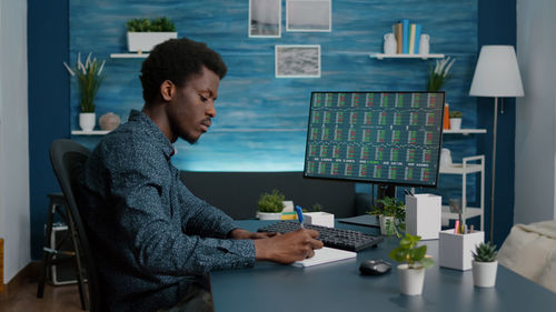 Side view of young man using phone while sitting on table