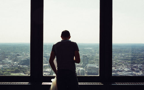 Rear view of man looking at out a window against sky