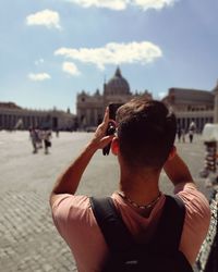 Rear view of woman photographing in city against sky