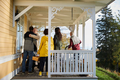Happy mature men embracing while standing on porch by friends