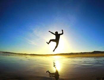 Full length of a woman jumping on beach at sunset