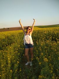 Full length of young woman standing amidst flowering plants on field