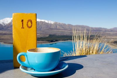 Coffee cup on table by lake against clear sky