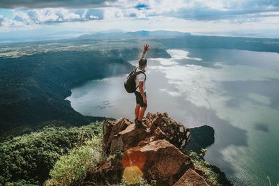 Man standing on rock by sea against sky