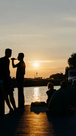 Silhouette people standing on shore against sky during sunset