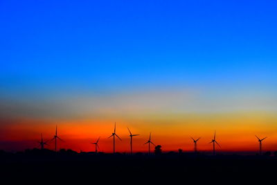 Silhouette wind turbines on land against sky during sunset