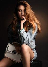 Portrait of young woman sitting against brown background