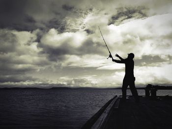 Side view of silhouette man fishing at calm sea