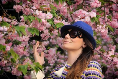 Low angle view of beautiful woman wearing sunglasses standing by cherry blossom in park