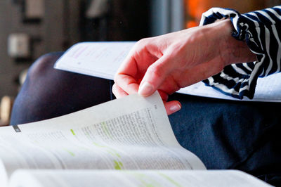 Midsection of woman with books sitting on sofa at home