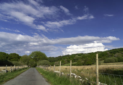 Empty road amidst field against sky