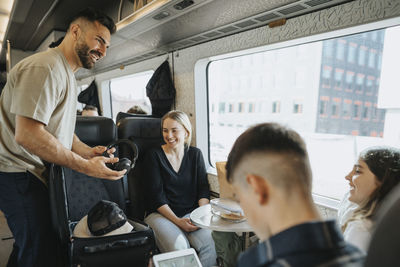 Smiling man removing headphones from suitcase while talking to family in train