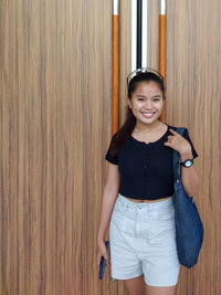 Portrait of smiling woman standing against wooden wall