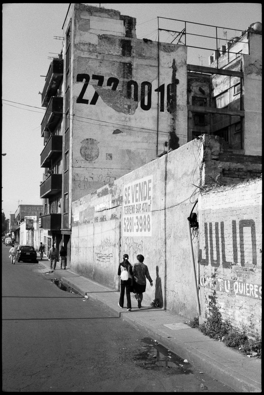 building exterior, architecture, city, built structure, street, text, transfer print, men, communication, real people, group of people, city life, walking, transportation, building, road, city street, people, auto post production filter, mode of transportation, outdoors