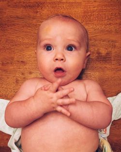 Surprised baby boy lying on wooden floor