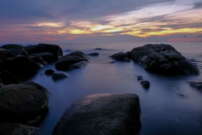 Rocks in sea against sky during sunset