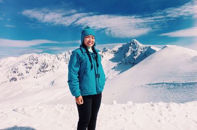 Portrait of smiling young woman standing on snowcapped mountain against sky