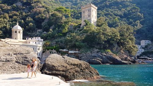 Mother with children walking on footpath by sea against mountain