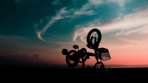 Silhouette bicycle at beach against sky during sunset