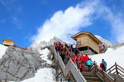 Low angle view of people on snowcapped mountain against sky