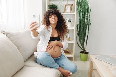 Young woman using mobile phone while sitting on sofa at home