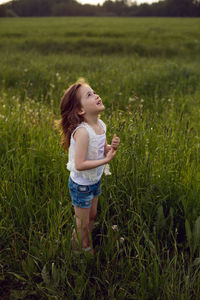 Child girl in a white t-shirt and denim shorts stands alone on a green field and waits