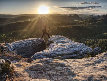 Photographer on mountain cliff above valley with morning mist hold tripod . hiker will take picture