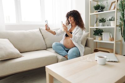 Young woman using phone while sitting on sofa at home