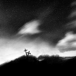 Silhouette cross on field against cloudy sky