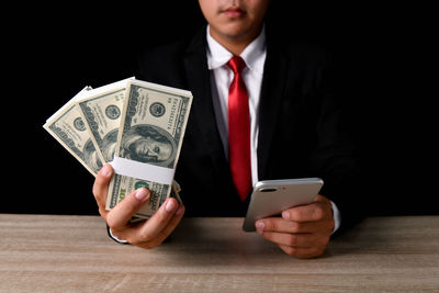 Midsection of businessman holding paper currency and phone on desk