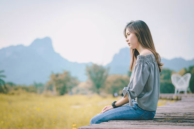 Young woman sitting on boardwalk against mountains