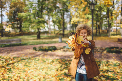 Portrait of woman holding leaves at park during autumn