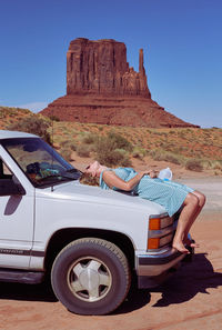 Full length of woman lying on car against rock formation