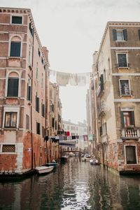 Boats moored in canal amidst buildings