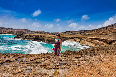 Full length of woman standing on rock against sky