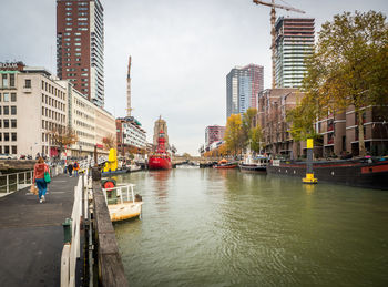 Boats in river by buildings in city against sky