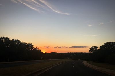 Road by silhouette trees against sky at sunset