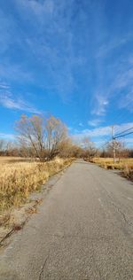 Surface level of road amidst landscape against blue sky