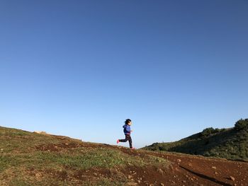 Boy running on mountain against clear blue sky