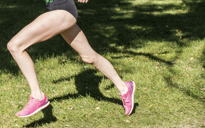 Low section of woman wearing pink shoes running on grass