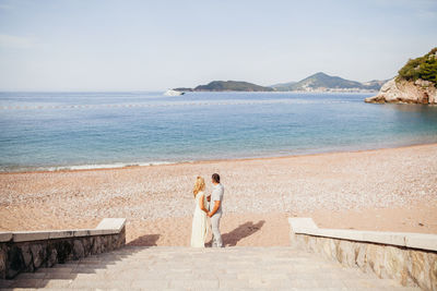 Rear view of couple standing at beach against sky