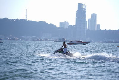 People riding on sea by city against sky