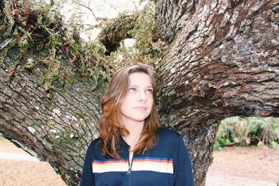 Portrait of beautiful young woman standing against tree trunk