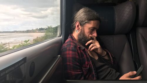 Thoughtful man using mobile phone while sitting in train