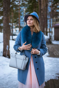 Beautiful woman in blue coat and hat posing outdoors in the snow