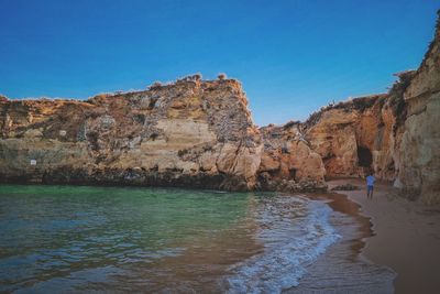 Rock formations on beach against clear blue sky