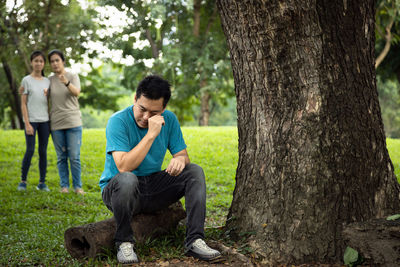 Rear view of men sitting on plant against trees