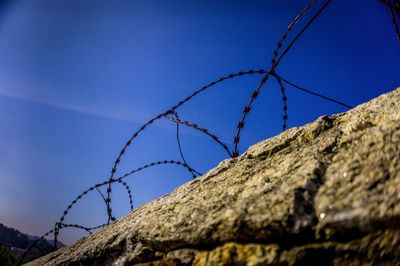 Low angle view of razor wire fence against blue sky