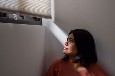 Woman looking away while standing against wall at home